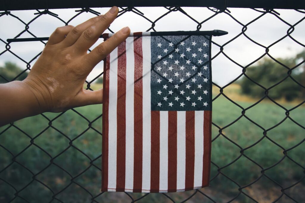 Hand holding america flag in front of a barbed fence. Illegal immigration concept.