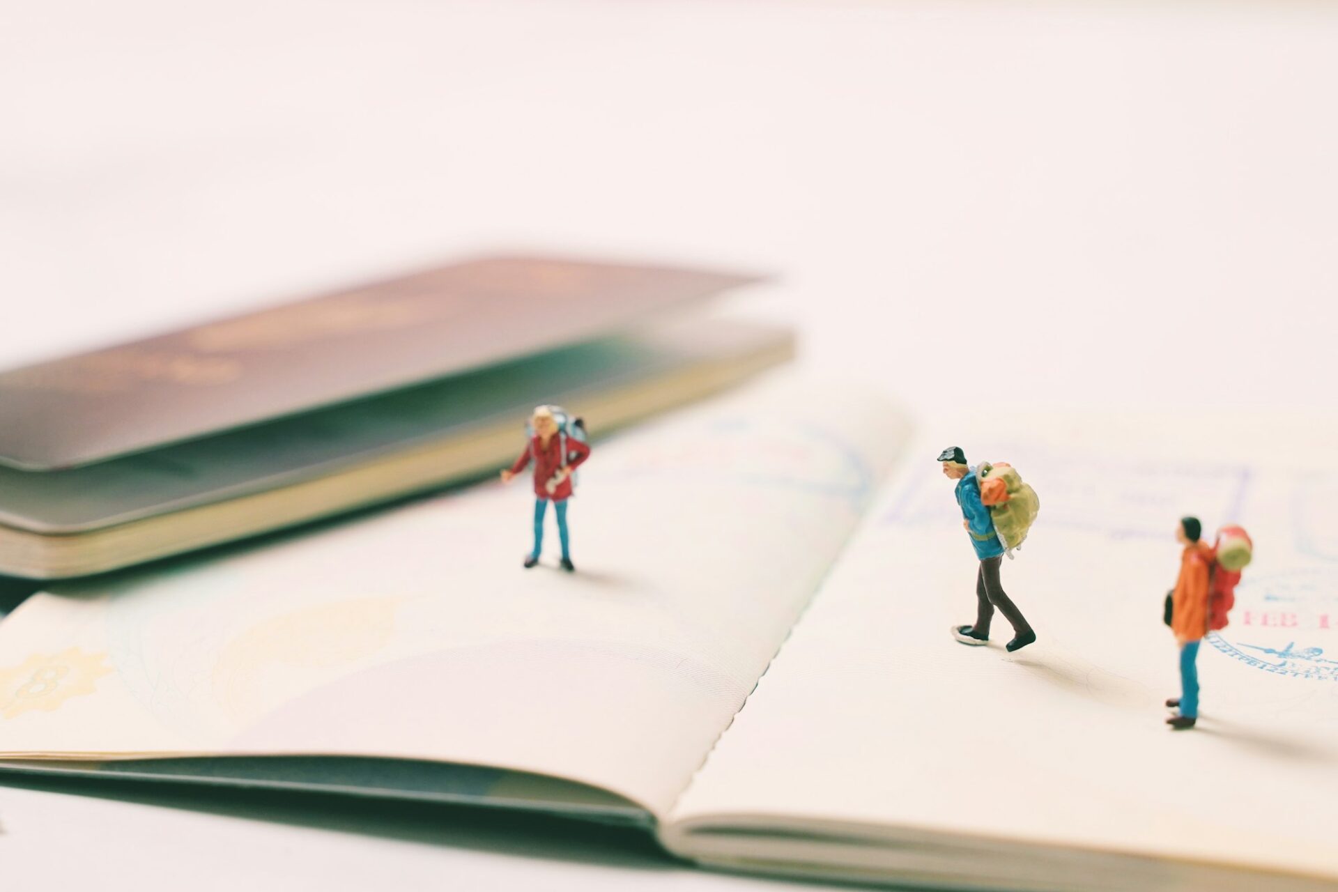 Miniature people figures with backpack walking and standing on passport page with immigration stamps